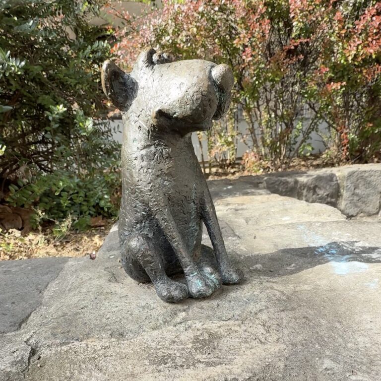 A small bronze dog sitting upright on a stone surface.